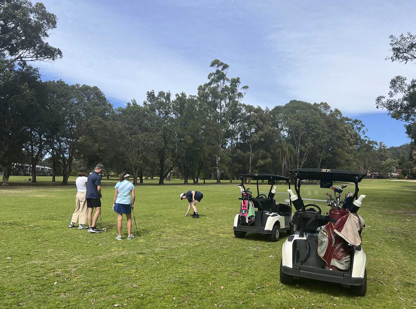 Four friends playing golf alongside two golf buggies at Leonay Golf Club Golf Course, surrounded by trees with the Blue Mountains in the background